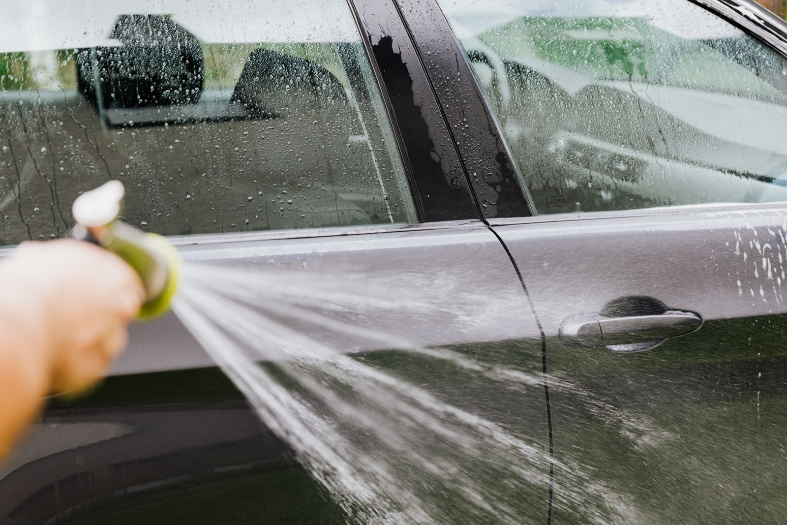 Volunteer rinsing a car with a hose at a charity wash