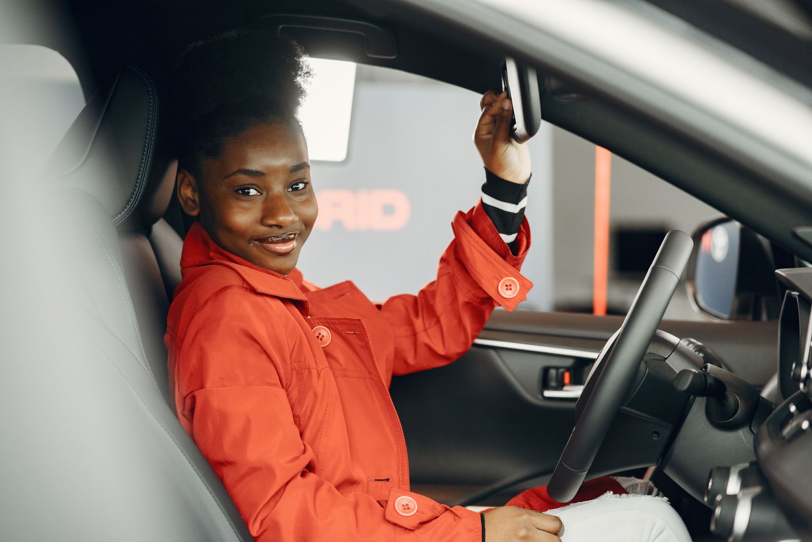 Smiling driver in a red jacket adjusting her mirror